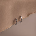 Silver huggie hoop earrings on a beige fabric background