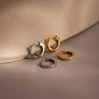 Two pairs of hoop earrings in gold and silver on a beige surface