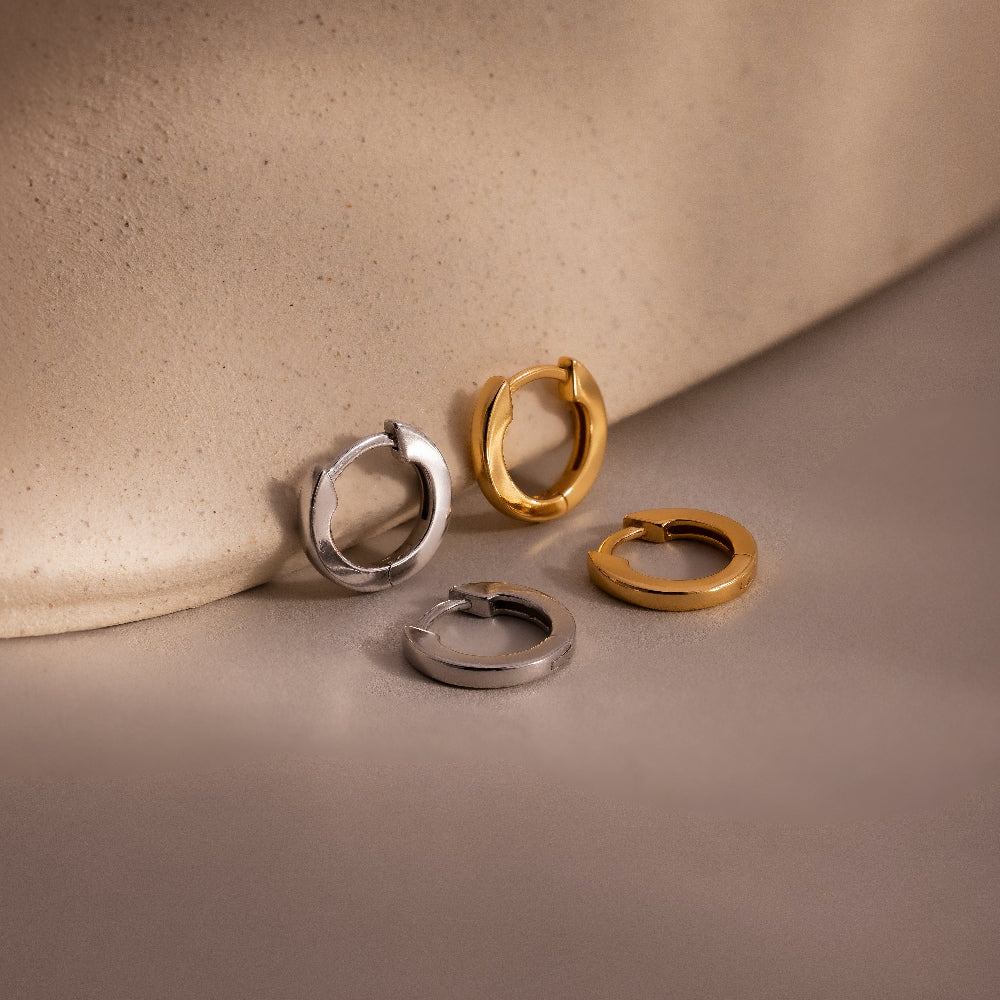 Two pairs of hoop earrings in gold and silver on a beige surface