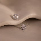 Pair of silver diamond stud earrings on a beige stone background
