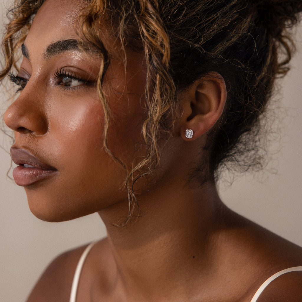 Close-up of a woman wearing silver diamond stud earrings against a neutral background
