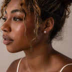 Close-up of a woman wearing silver diamond stud earrings against a neutral background