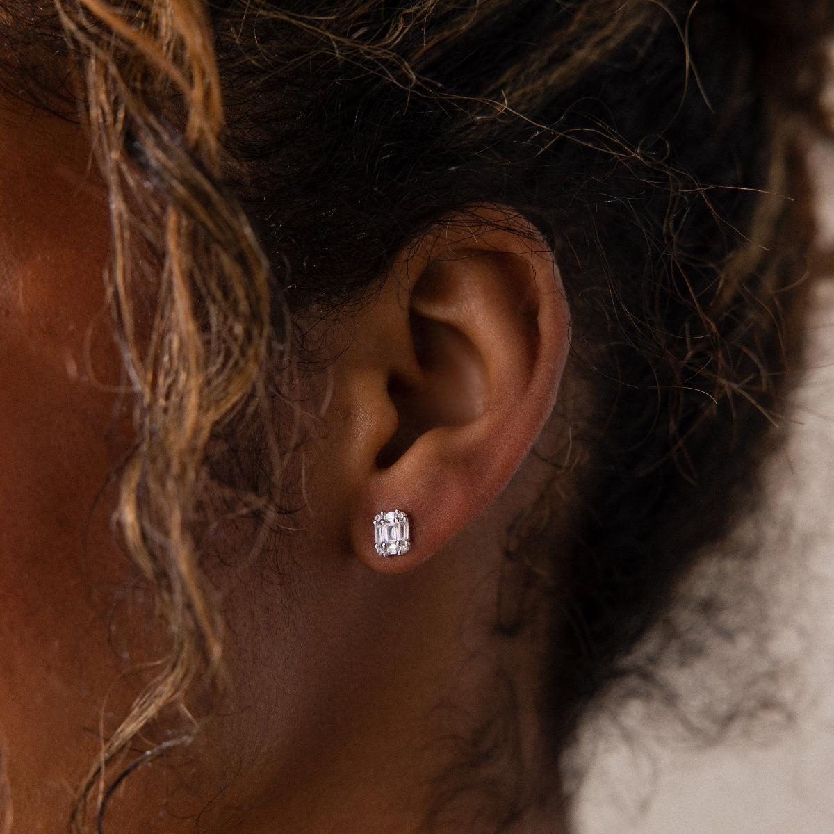 Close-up of a model wearing a silver diamond stud earring with braided hair.