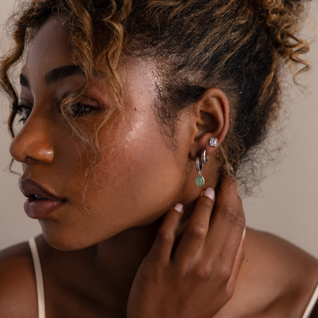 Woman wearing various silver earrings with a neutral background