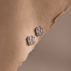 Pair of silver emerald-cut clear gemstone earrings on a beige fabric surface