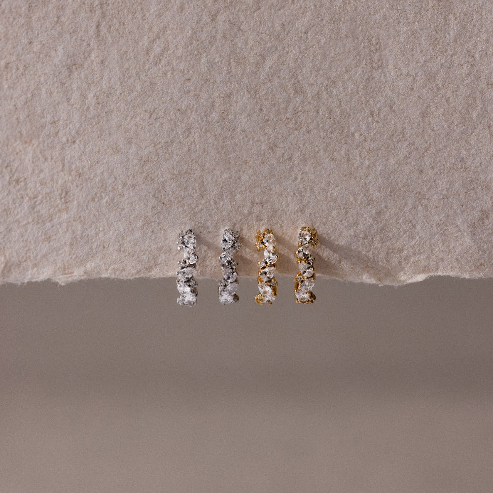 Four dainty diamond cluster huggie hoop earrings, on a textured beige surface