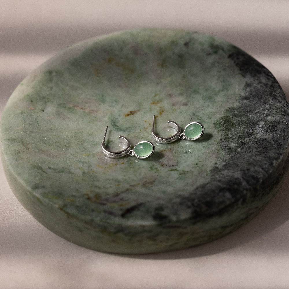 Pair of silver stud hoop earrings with green jade drop pendants on a green stone surface