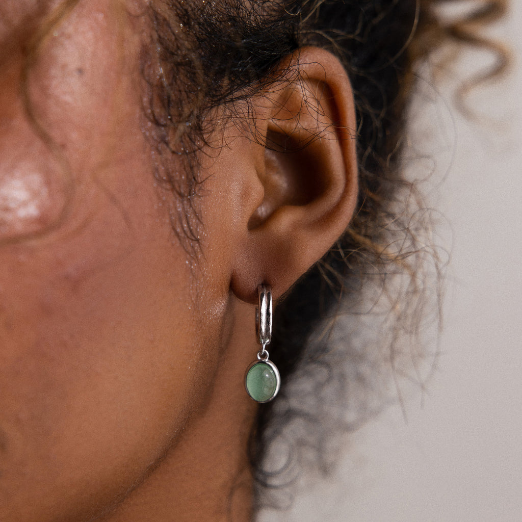 Close-up of a model wearing a silver hoop earring with a green gemstone.