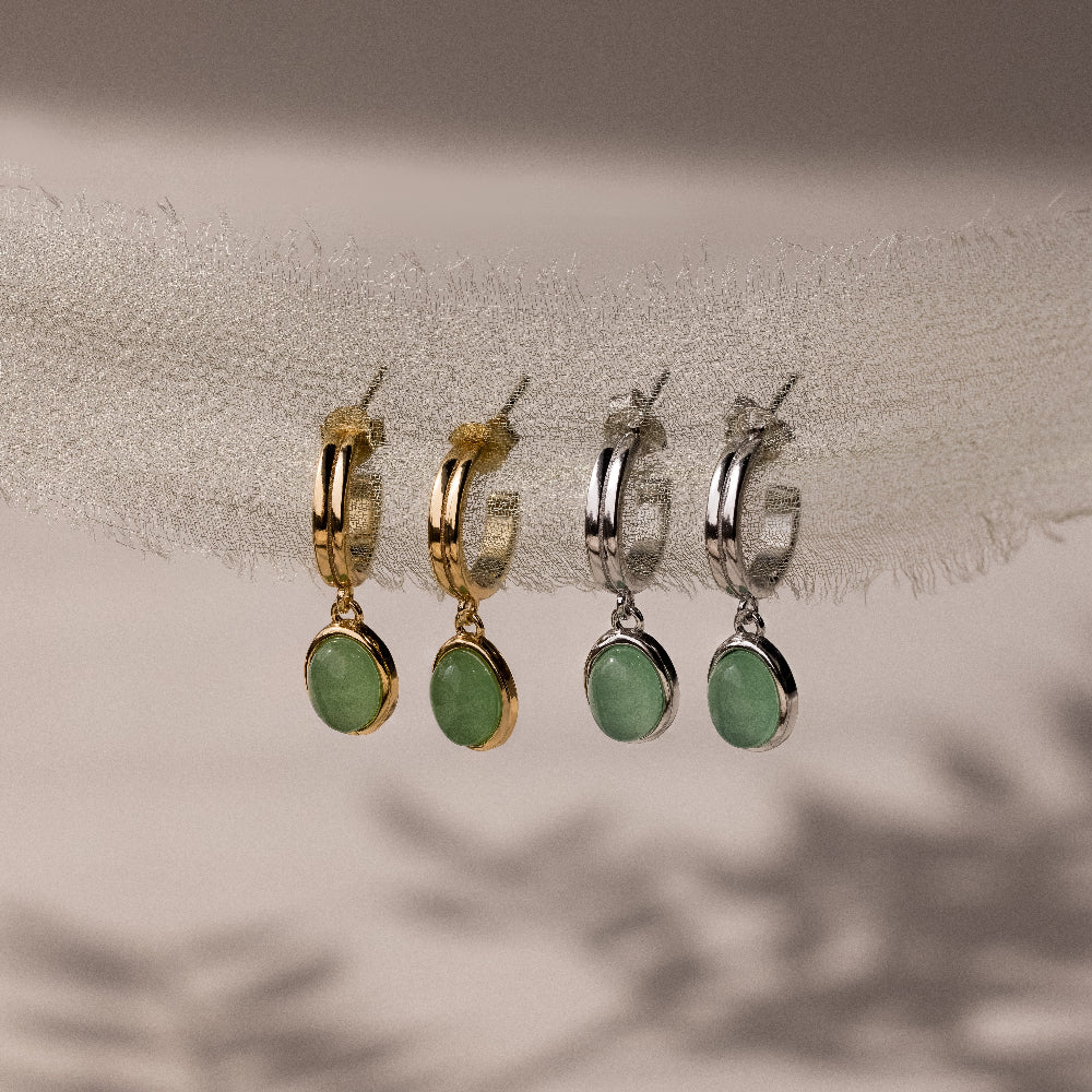 Two pairs of hoop earrings in gold and silver with green jade drop stones on a neutral background