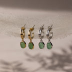 Two pairs of hoop earrings in gold and silver with green jade drop stones on a neutral background