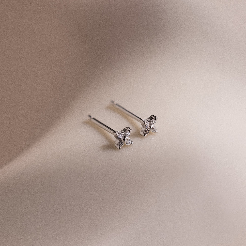Pair of silver stud earrings with star-shaped diamond elements on a beige background