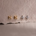 Two pairs of gold and silver star-shaped diamond stud earrings on a textured beige surface