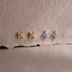 Two pairs of gold and silver star-shaped diamond stud earrings on a textured beige surface