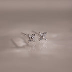 Pair of silver stud earrings with small diamonds on a reflective surface.
