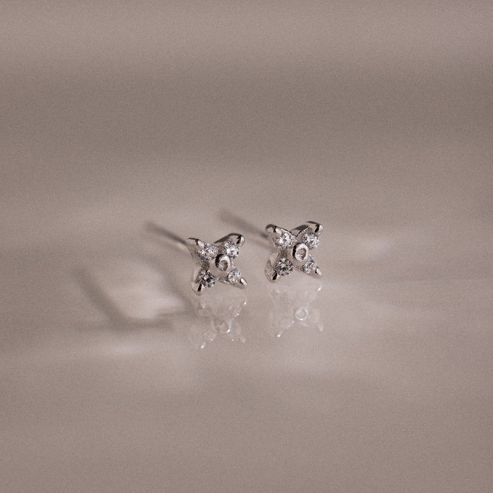 Pair of silver stud earrings with small diamonds on a reflective surface.