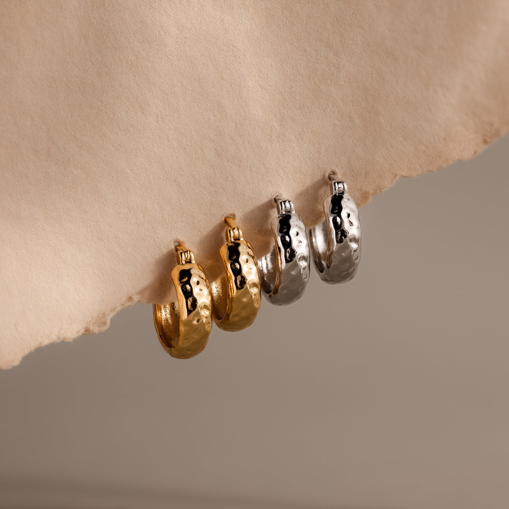 Two pairs of Bold Hammered Huggies earrings, one gold and one silver, displayed on beige paper—an ideal minimalist jewelry addition.