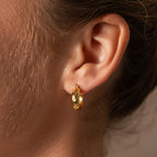 A close-up of an ear wearing Bold Hammered Huggies, highlighting this minimalist earring’s bold, textured gold finish.