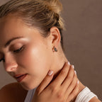 A woman with blonde hair in a bun touches her neck, wearing a white top and Bold Hammered Huggies in Silver that add a touch of minimal design to her look.