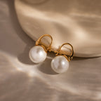 The Pearl Dome Drop Earrings feature lustrous pearls and a classic design, showcased on a smooth beige surface with soft lighting to highlight their timeless elegance.