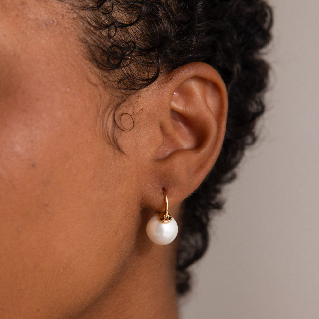 Close-up of a person's ear wearing Pearl Dome Drop Earrings—gold hoops accented with luminous pearls for an elegant, timeless look.