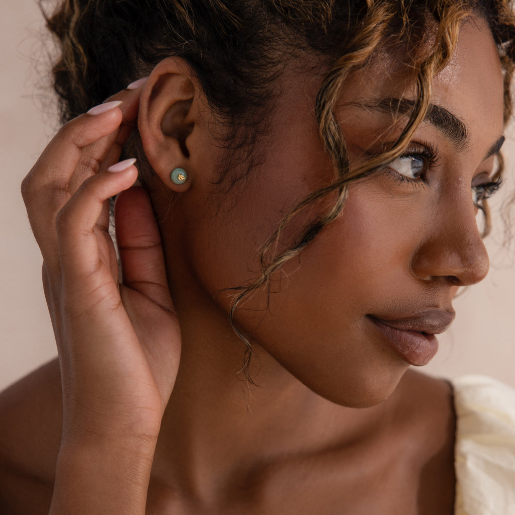 Model wearing gold Jade Bird Studs with dainty golden dove birds on round green jade discs.