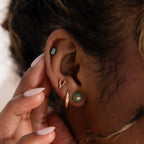 Model wearing a gold Jade Bird Stud Earring with a dainty golden dove bird on a round green jade disc, stacked with multiple gold and jade stud earrings.