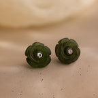 Close-up of the jade rose studs on a textured neutral surface, showing fine carved petals and crystal centers in detail.
