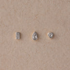 The Diamond Bezel Flatback Studs Set in Silver features rectangular, teardrop, and triangular gemstones on a beige textured background for a classic, elegant look.