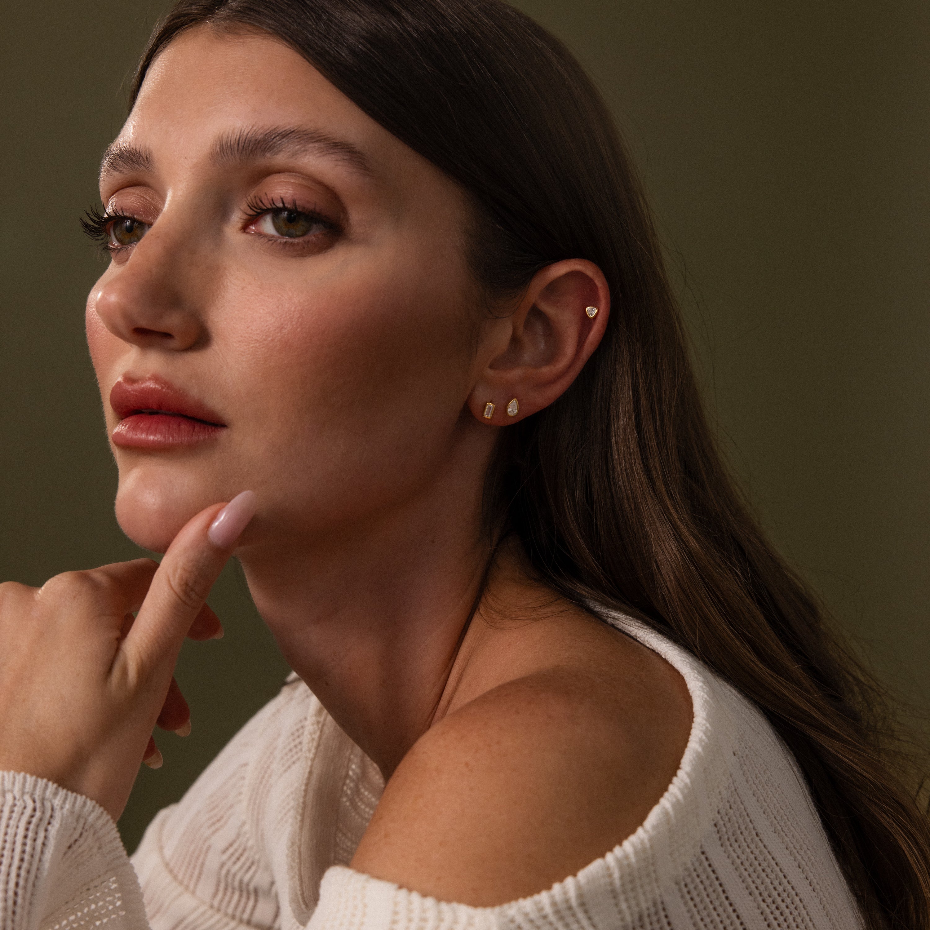 Woman with long brown hair gazing sideways, wearing a white off-shoulder top and Diamond Bezel Flatback Studs Set in 18K Gold.