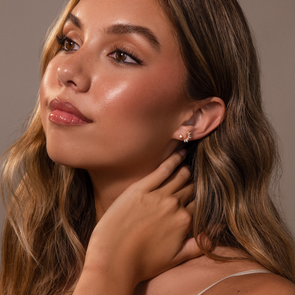 Woman with long wavy hair and glowing skin wears Baby Venus Flatback Studs, featuring a floral backing, as she looks upward with her hand near her neck.