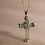 Silver chain necklace with a jade cross pendant, accented by polished gold end caps and an X shaped detail at the center.