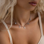 Model wearing a silver heart charm necklace featuring five unique heart pendants, styled with a neutral tank top.