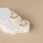 Gold cursive name earrings on a textured white surface with a beige background