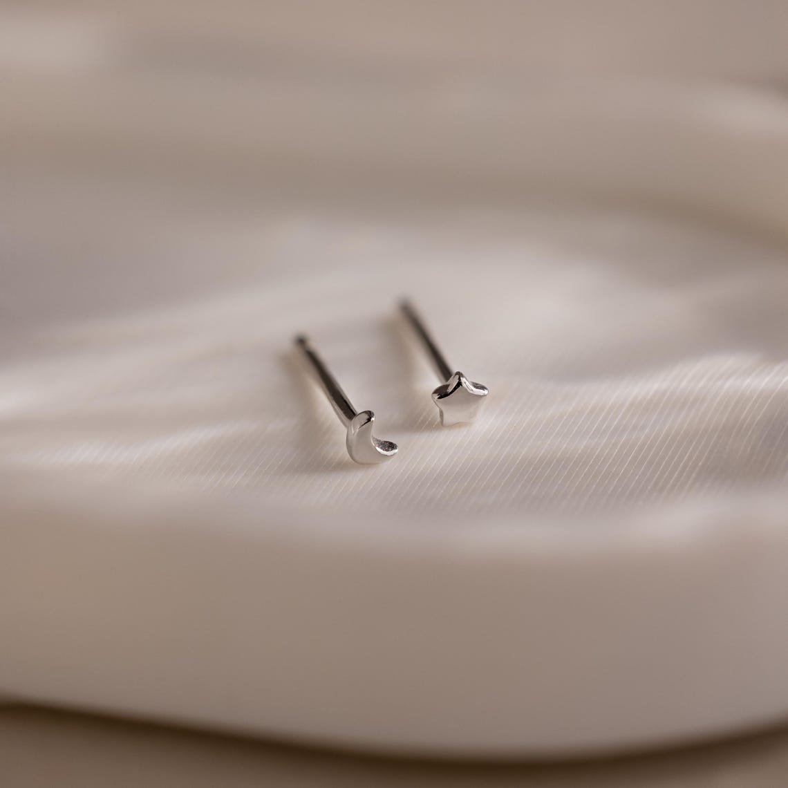 Silver moon and star-shaped earrings on a textured beige jewelry dish