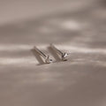 Pair of tiny silver moon and star earrings on a beige fabric background