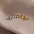 Two pairs of star-shaped earrings in gold and silver on a neutral background