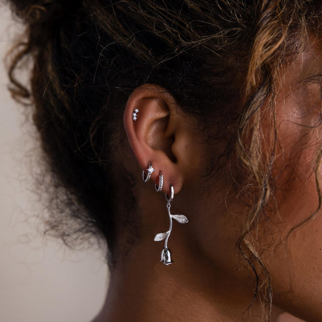 Close-up of an ear with multiple silver earrings against a neutral background