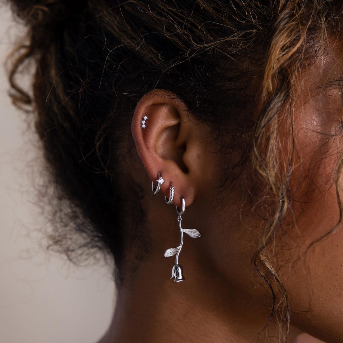 Close-up of an ear with multiple silver earrings against a neutral background