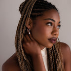 Woman with braided hair and a silver pearl hoop earring touching her face against a neutral background