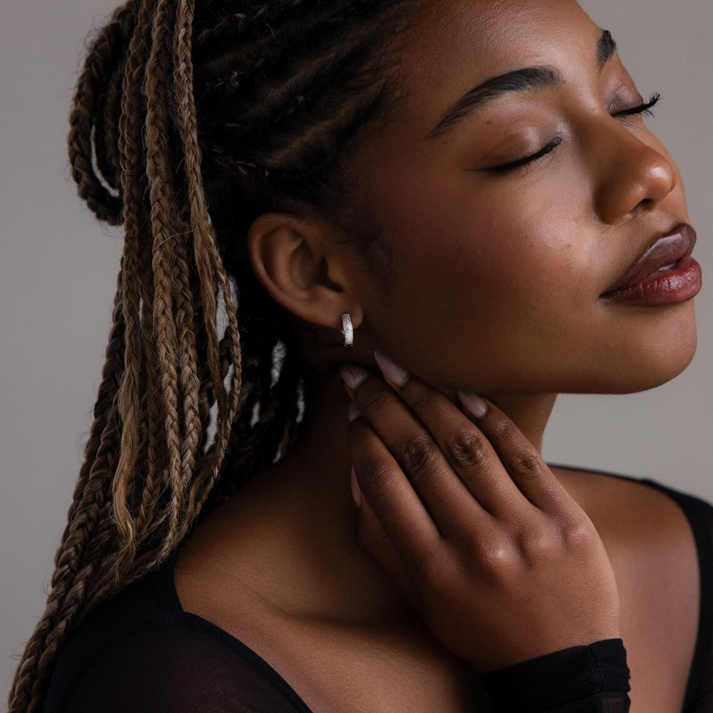 Woman with braided hair wearing a small pave diamond earring, looking away from the camera.