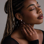Woman with braided hair wearing a small pave diamond earring, looking away from the camera.