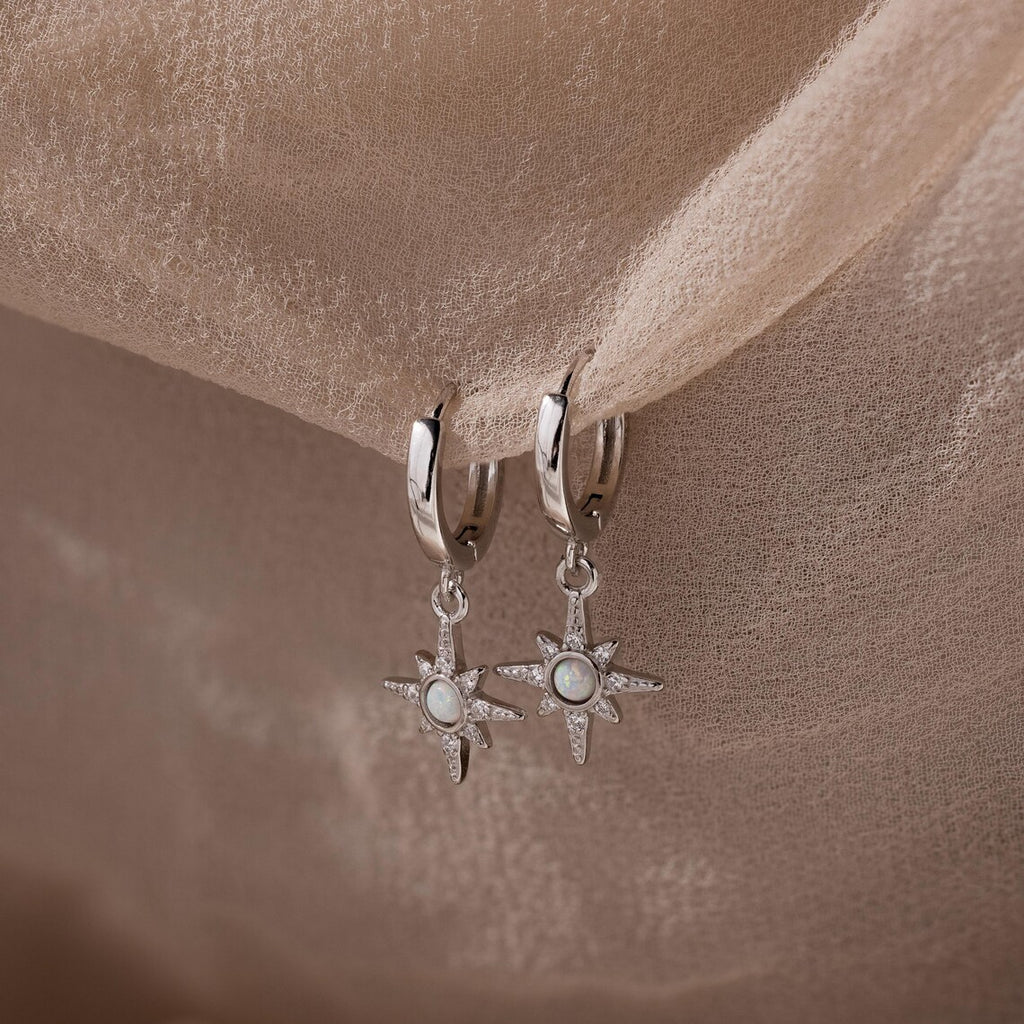Pair of hanging silver opal hoop earrings with star designs on a beige fabric background