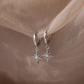 Pair of hanging silver opal hoop earrings with star designs on a beige fabric background