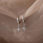 Pair of hanging silver opal hoop earrings with star designs on a beige fabric background