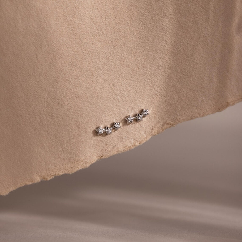 Pair of silver diamond stud earrings on a beige fabric background