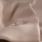 Pair of silver star stud earrings with clear stones on a beige fabric background