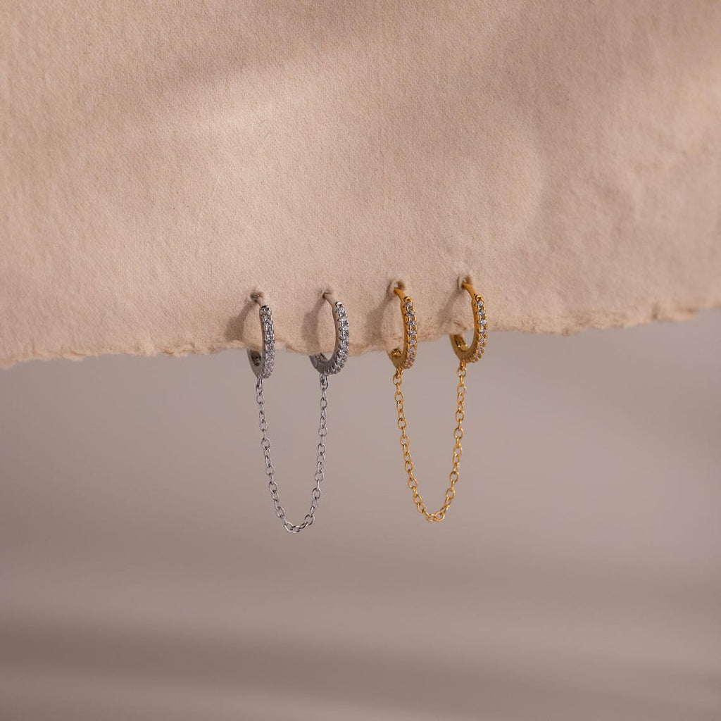Two sets of hoop earrings in gold and silver with chain details on a beige background
