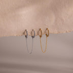 Two sets of hoop earrings in gold and silver with chain details on a beige background