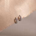 Pair of silver clear gemstone hoop earrings on a beige fabric background