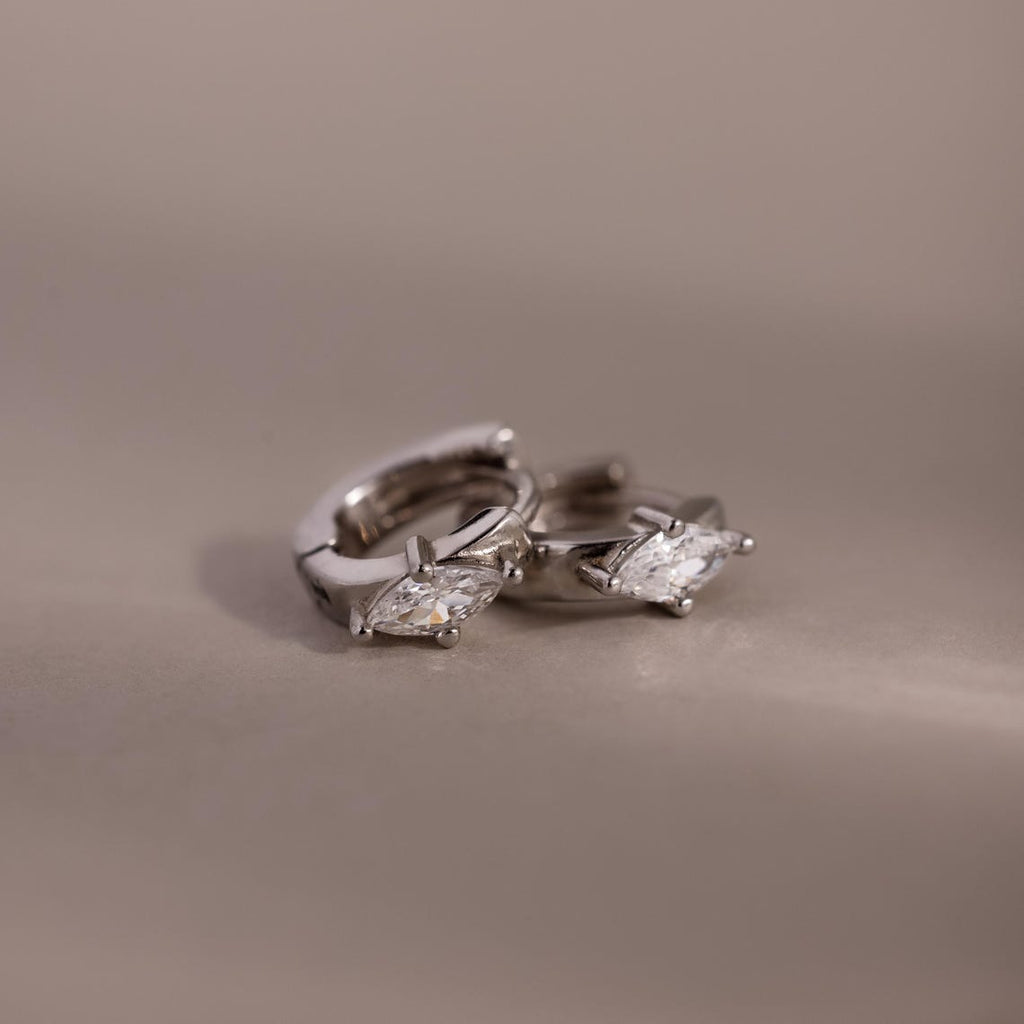 Pair of silver hoop earrings with marquise-shaped gemstones on a beige background
